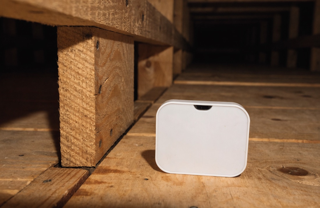 A digital humidity gauge resting on the plywood subfloor decking of a crawl space beside wooden framing